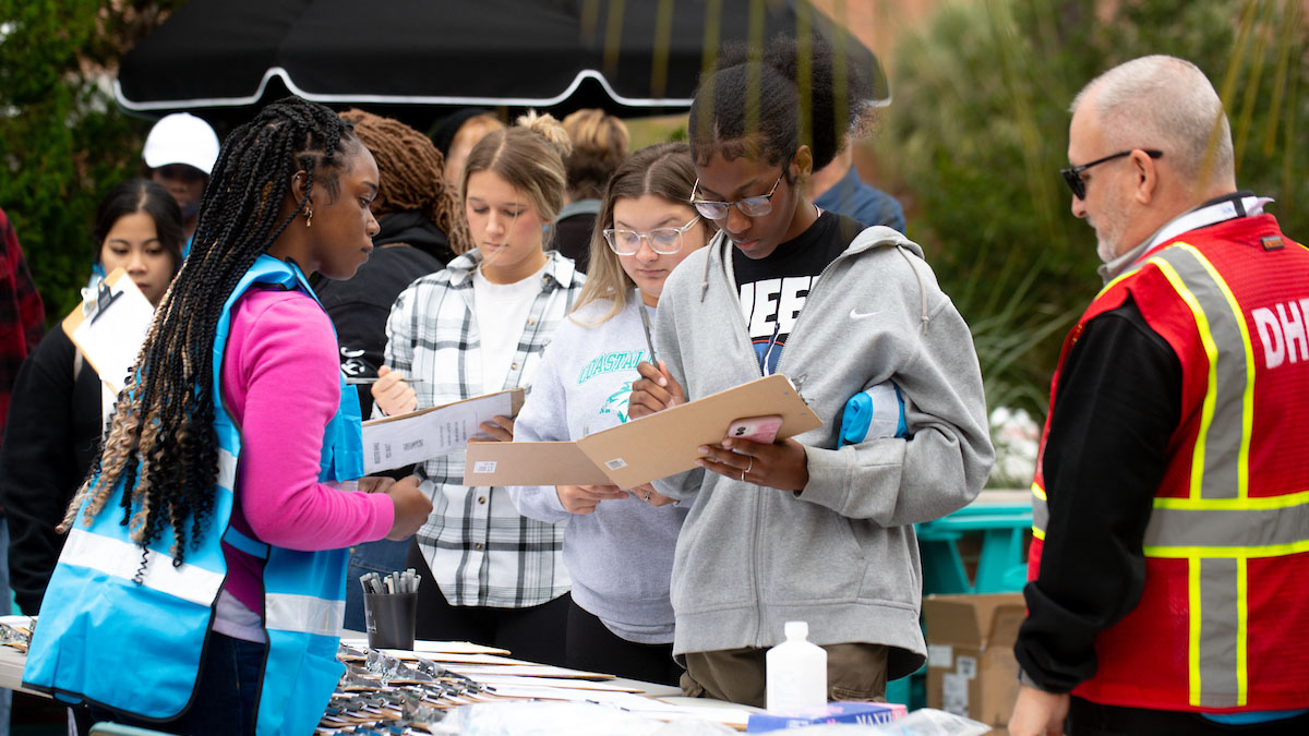 Students gather at an outdoor table to collect information and complete forms during a community health outreach or data‑collection activity.